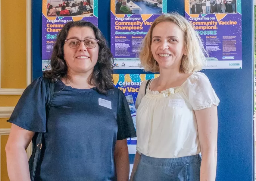 Alida and Cecilia posing in front of community vaccine champions poster display