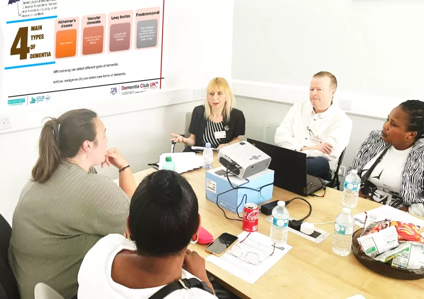 Five people sitting around a table, having a discussion about dementia using worksheets and laptops