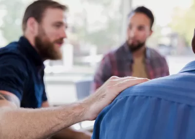 men sitting together facing away from camera, one man with hand on shoulder of other man