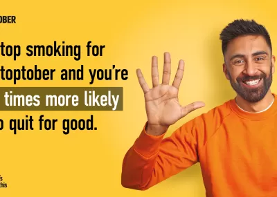 Man in orange jumper smiling with hand raised, text says 'stop smoking for stoptober and your 5 times more likely to quit for good'.