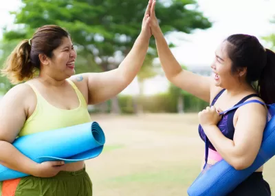 two women with yoga mats clapping
