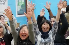 women laughing while doing seated exercises with arms in air