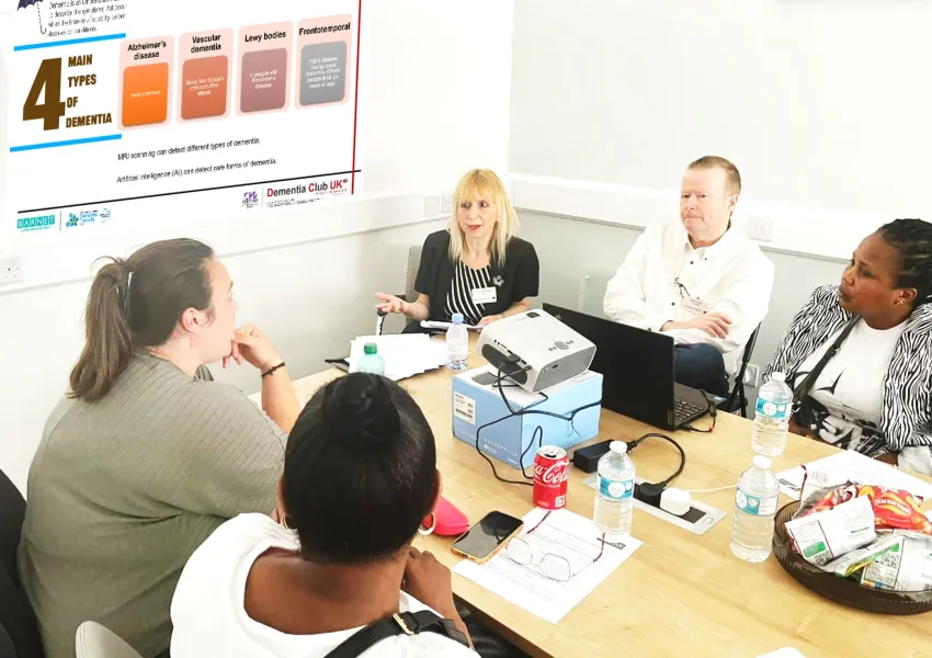 Five people sitting around a table, having a discussion about dementia using worksheets and laptops