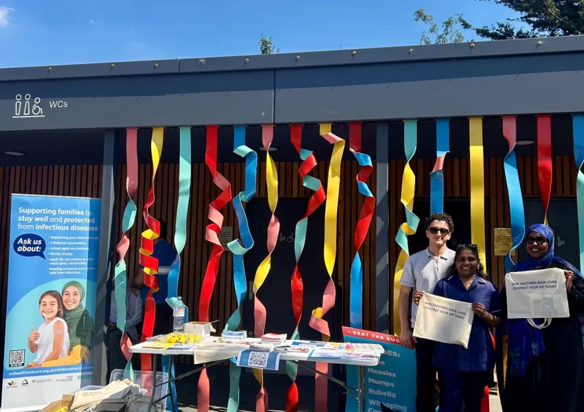 Three people standing next to the vaccination stall holding totebags.