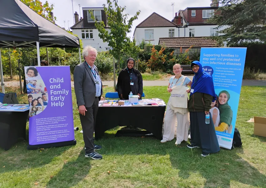 People infront of a stand displaying information about childhood vaccinations.