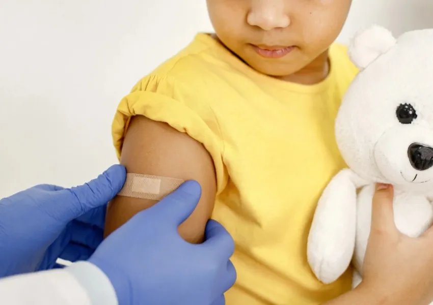 A child having a plaster put on. The child is holding a cuddly toy.