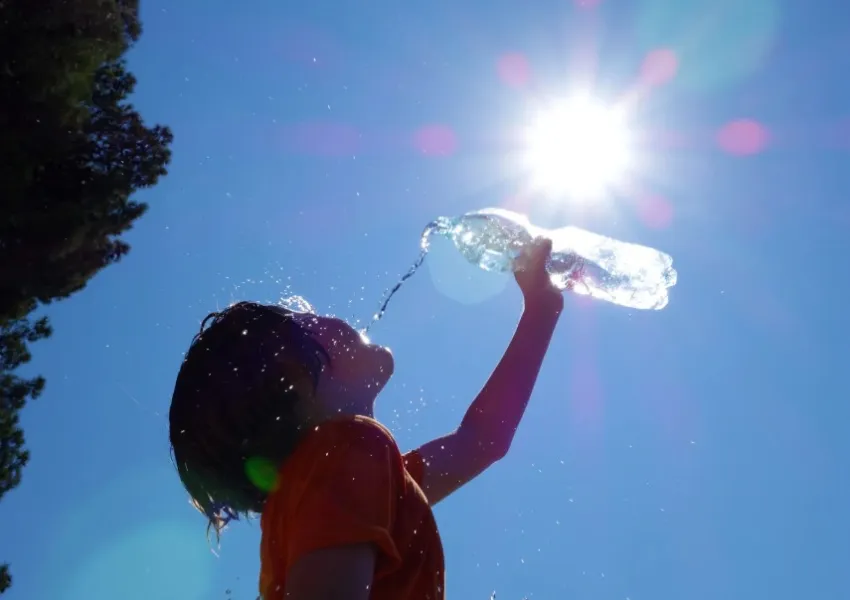 A child drinking water from a bottle, with blue sky, and the sun shining.
