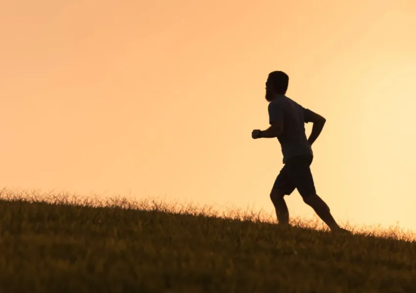The silhouette of a man who appears to be running on a grassy area.