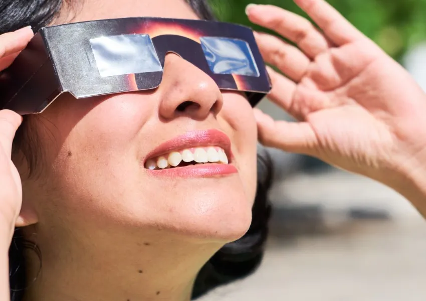 A person, looking up at a solar eclipse, while wearing safety glasses.