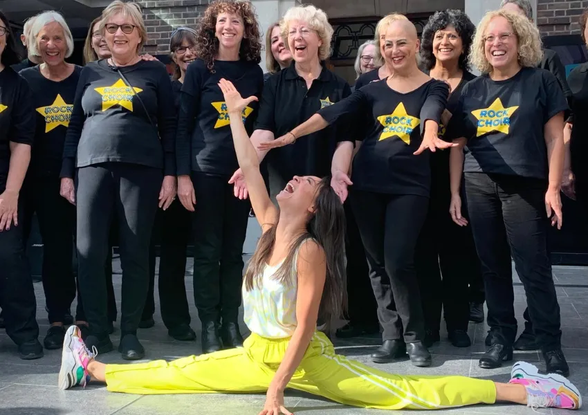 A dance group with matching black tshirts with gold stars pose for a photo with a dancer posing in split position on the floor in front of them