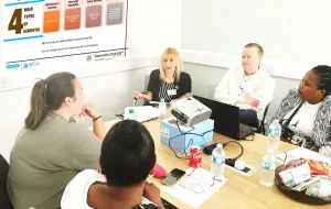 Five people sitting around a table, having a discussion about dementia using worksheets and laptops
