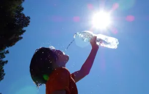 A child drinking water from a bottle, with blue sky, and the sun shining.