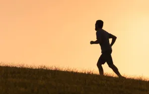 The silhouette of a man who appears to be running on a grassy area.
