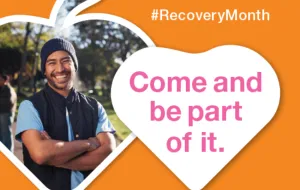 Smiling man in beanie, outside on sunny day. Orange background, pink writing in white heart 'come and be part of it'. #RecoveryMonth