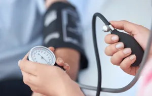 An arm with a blood pressure monitor attached, and two hands performing the blood pressure check.