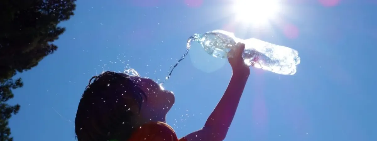 A child drinking water from a bottle, with blue sky, and the sun shining.
