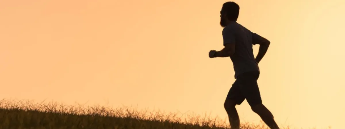 The silhouette of a man who appears to be running on a grassy area.