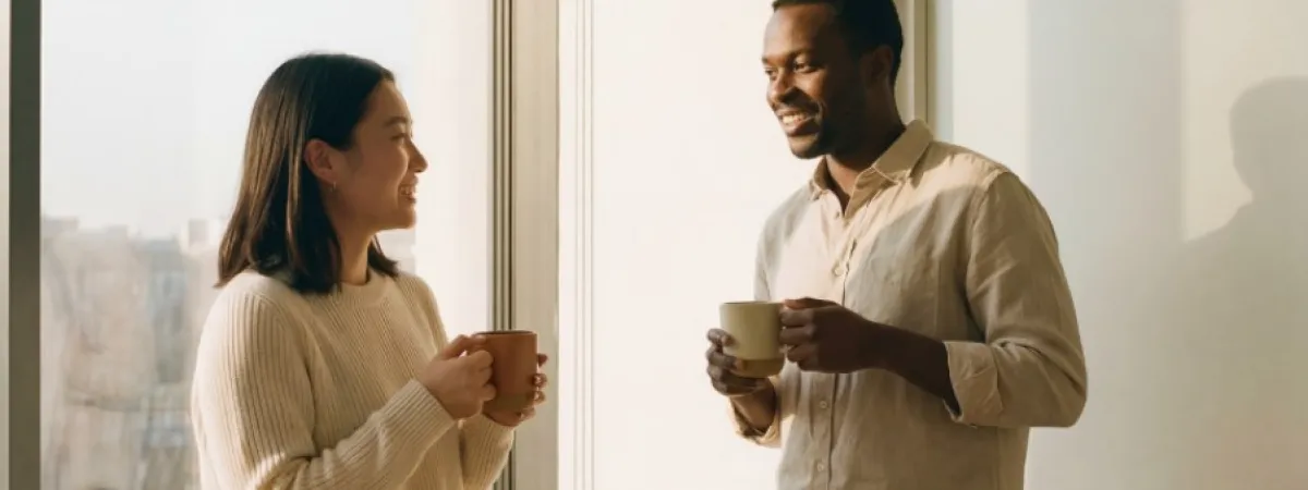 Two people, each holding a mug, talking and smiling.